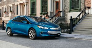 A blue 2019 Chevrolet Volt parked on the street outside of a townhouse