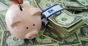 Placing coins in a piggy bank, with stacks of $1 bills in the background