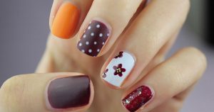 A closeup of a woman's nails with five different designs, one on each finger